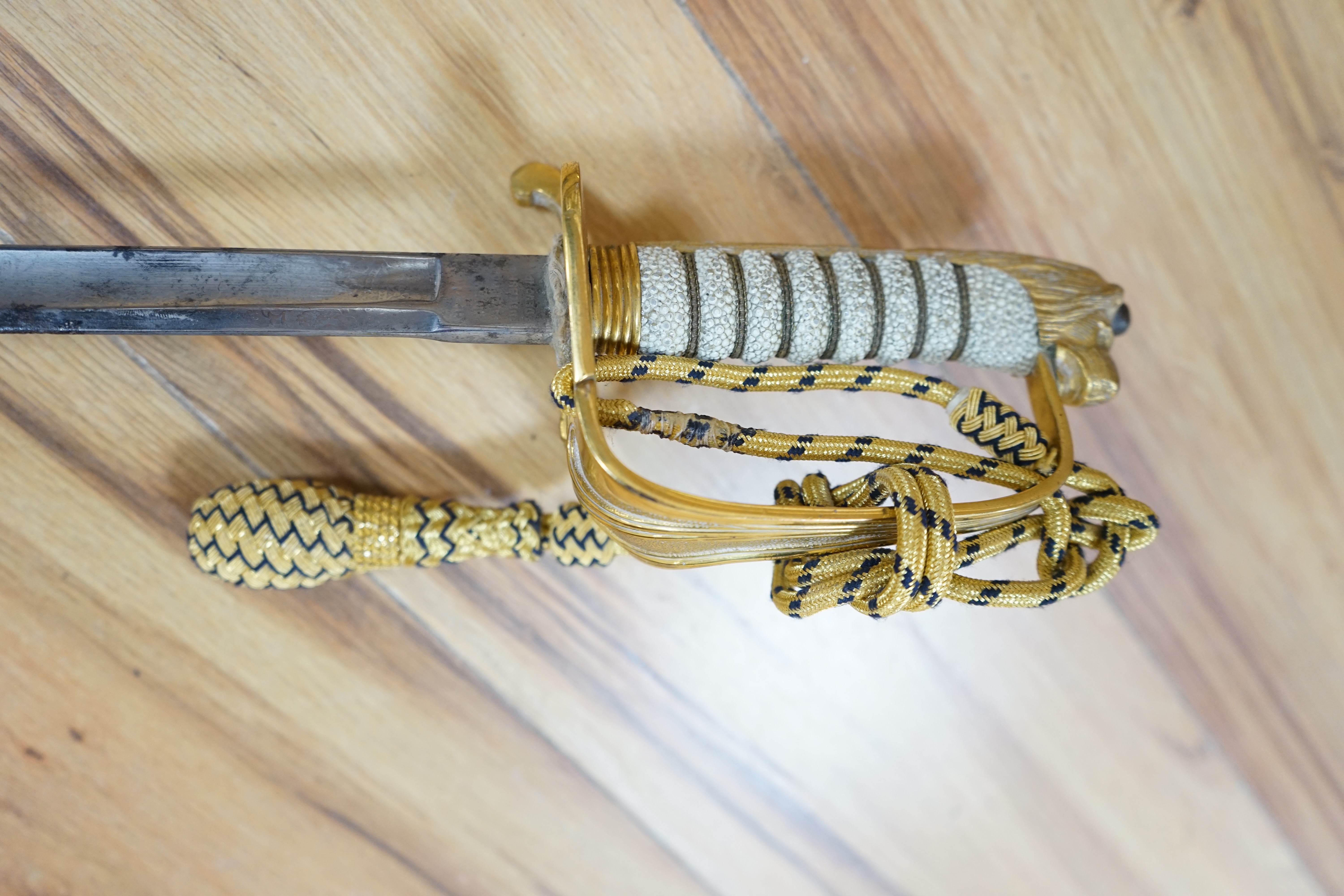 A Victorian Royal Navy officer’s sword by Grieves, engraved blade, lion’s head pommel, fish skin grip, folding guard engraved with R.J. Murray, with its sword knot and leather scabbard with brass mounts, blade 79cm. Cond